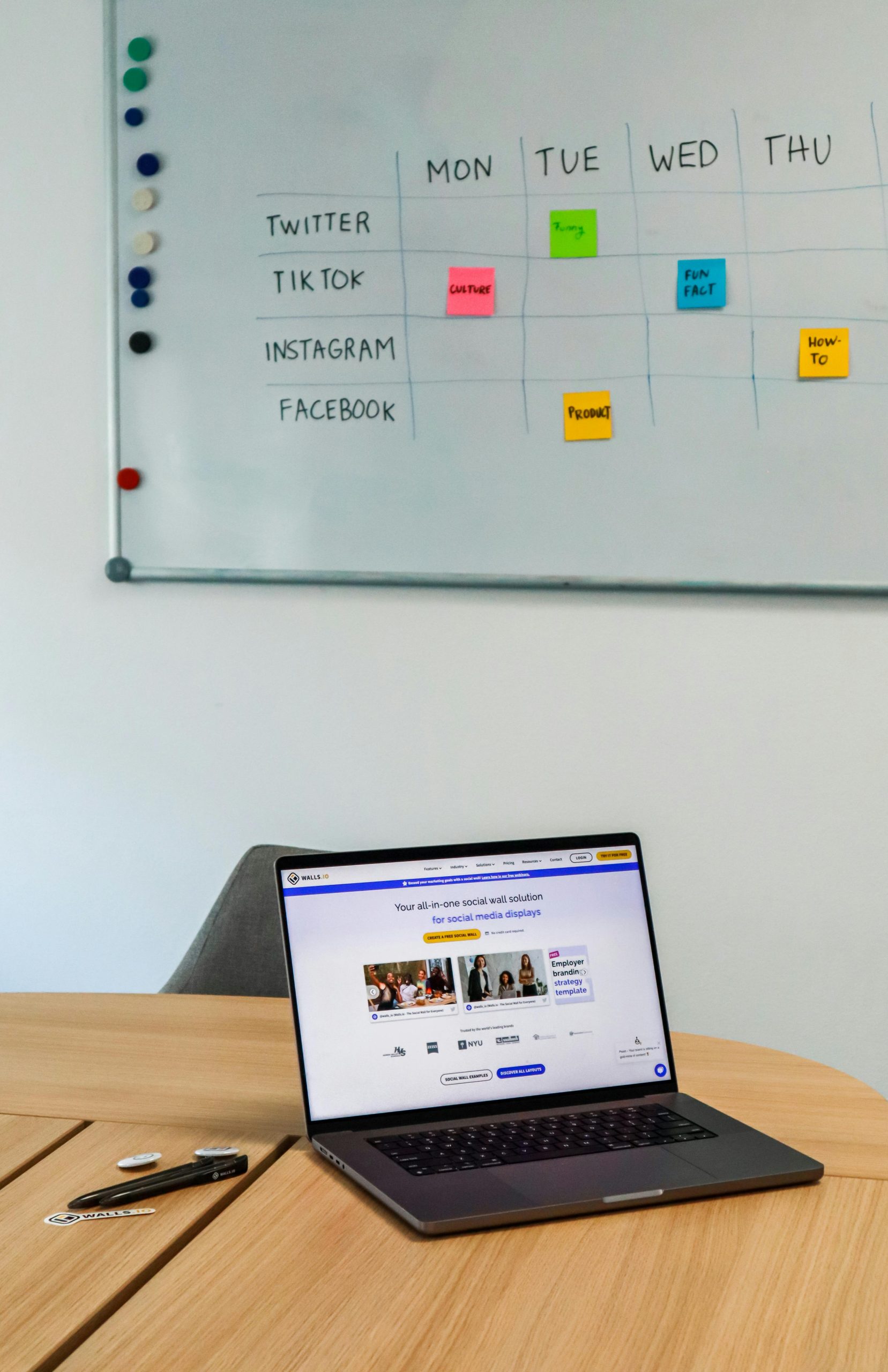 A physical social media content calendar on a whiteboard for Twitter, TikTok, Instagram, and Facebook, next to a laptop displaying a digital marketing website.