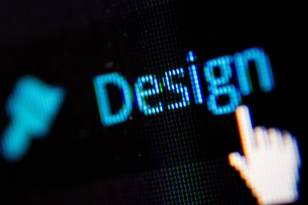 A close-up of a computer screen showing the word 'Design' in glowing blue text, with a white, pixelated cursor hand pointing at the 'n'