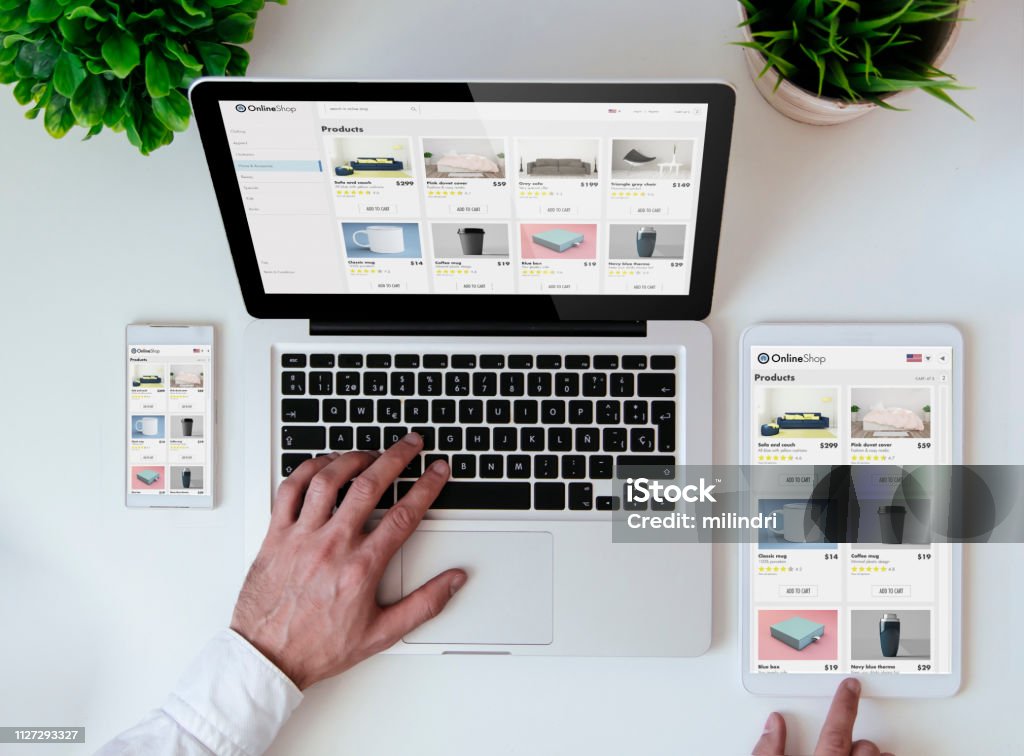 "Overhead shot of a person using a laptop, with a smartphone and tablet showing the same e-commerce 'OnlineShop' product page."