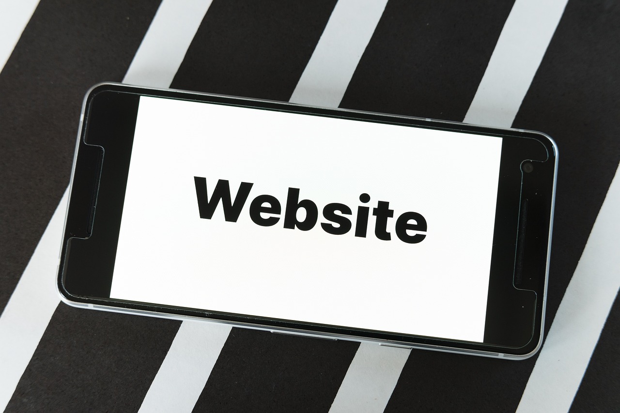 "Smartphone on a black and white striped surface, displaying the word 'Website' in bold black text on a bright, white screen."
