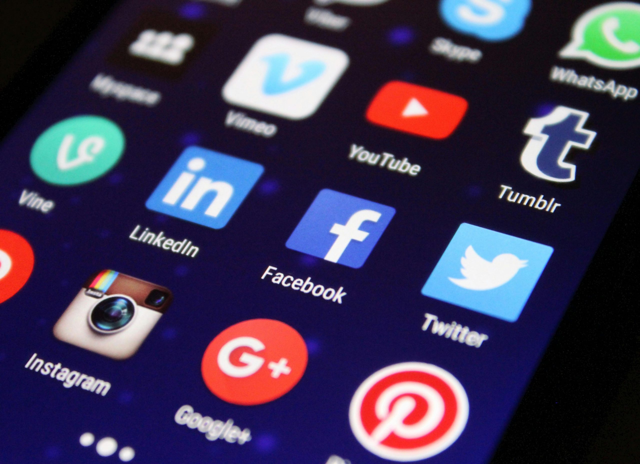 A close-up of a smartphone screen showing various social media and app icons including Facebook, YouTube, LinkedIn, Twitter, and Instagram.